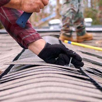 A roofer secures a row of shingles on a roof.