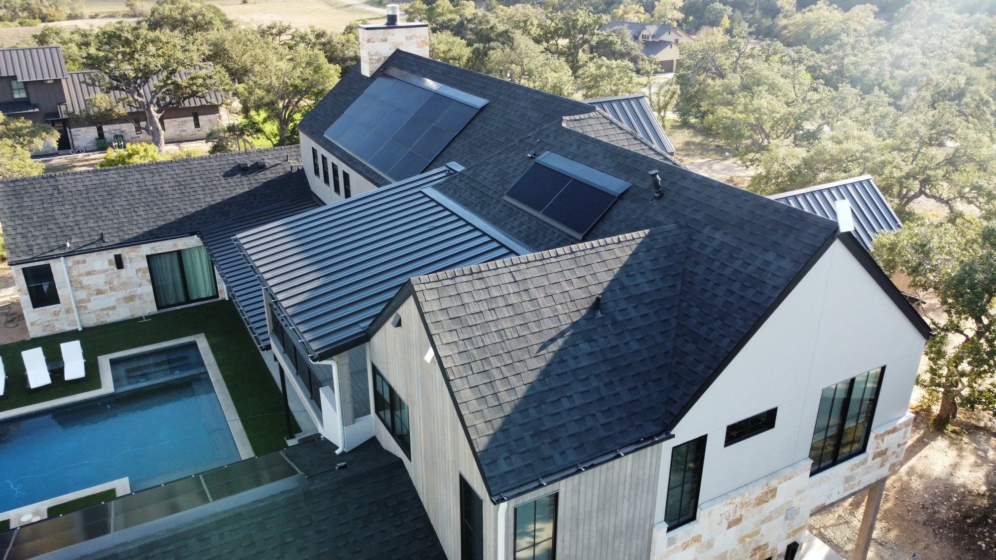 Aerial view of luxury home with premium roofing by Divided Sky — standing seam metal, architectural shingles, and solar panels in the Texas Hill Country