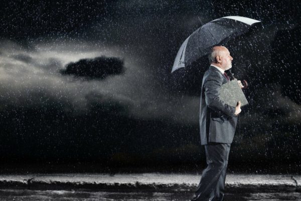 A man with an umbrella stands under a dark cloudy sky.