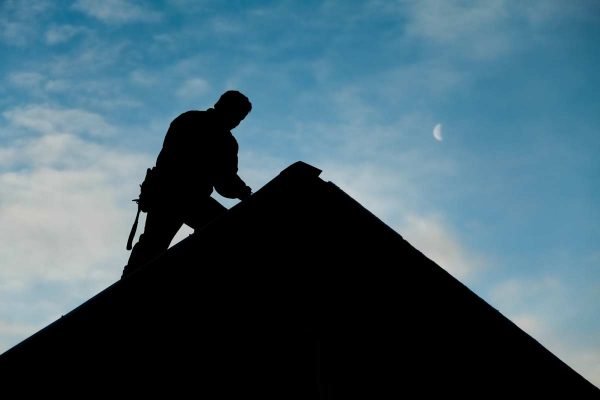 A roofer conducts a roof inspection silhouetted against an evening sky. roofing san marcos