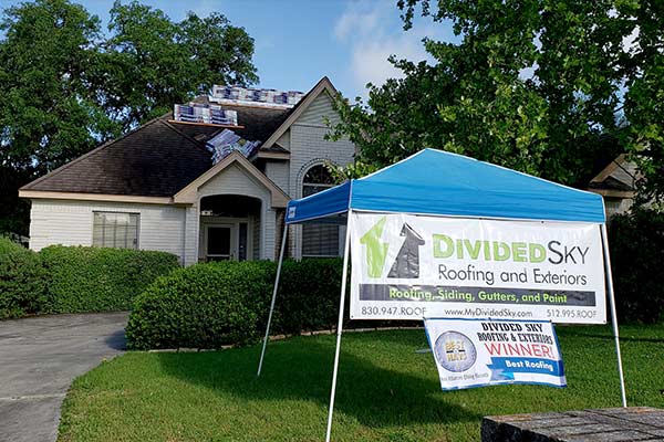 A Divided Sky sign is posted in the lawn of a house with roof work in progress.