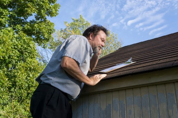 An insurance agent on their phone inspecting a roof for damage.