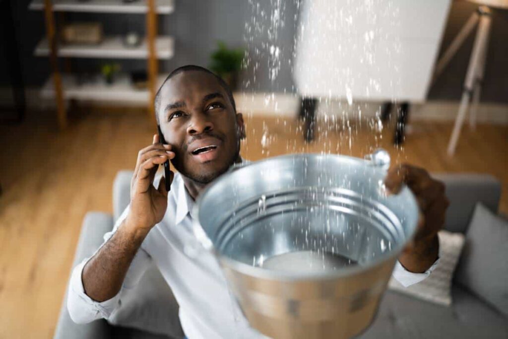 A man calling Seguin Roofers about a leak while catching water in a bucket in his home.