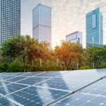 Solar panels sit on a commercial lot with a downtown city skyline as the backdrop.