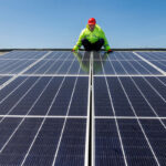 A worker is installing solar panels on a commercial roof.