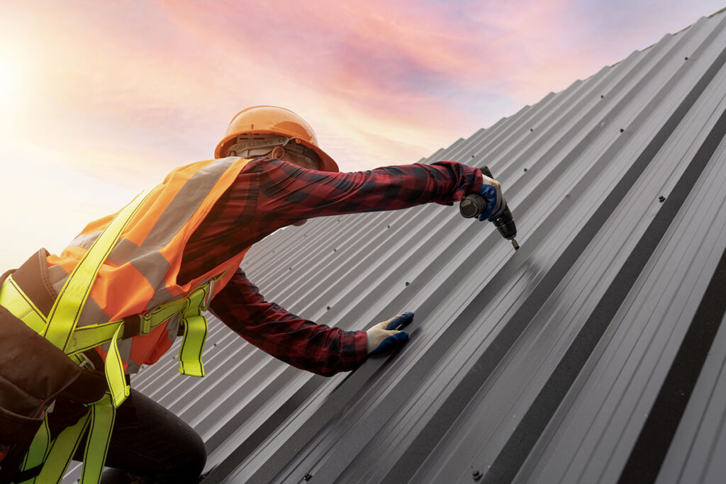 A worker installs metal roofing in Austin at sunset.